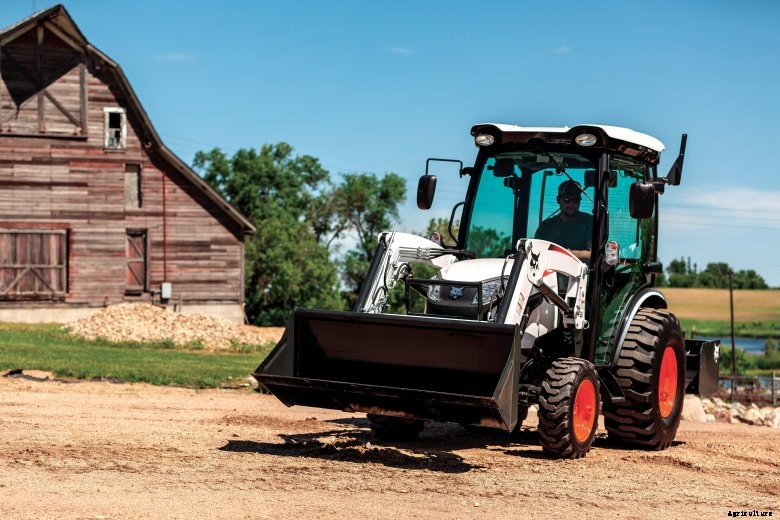 Bobcat compact tractor with a loader driving through a barnyard